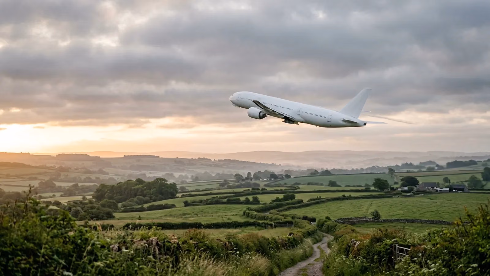 Widebody jet climbing over green countryside at sunrise